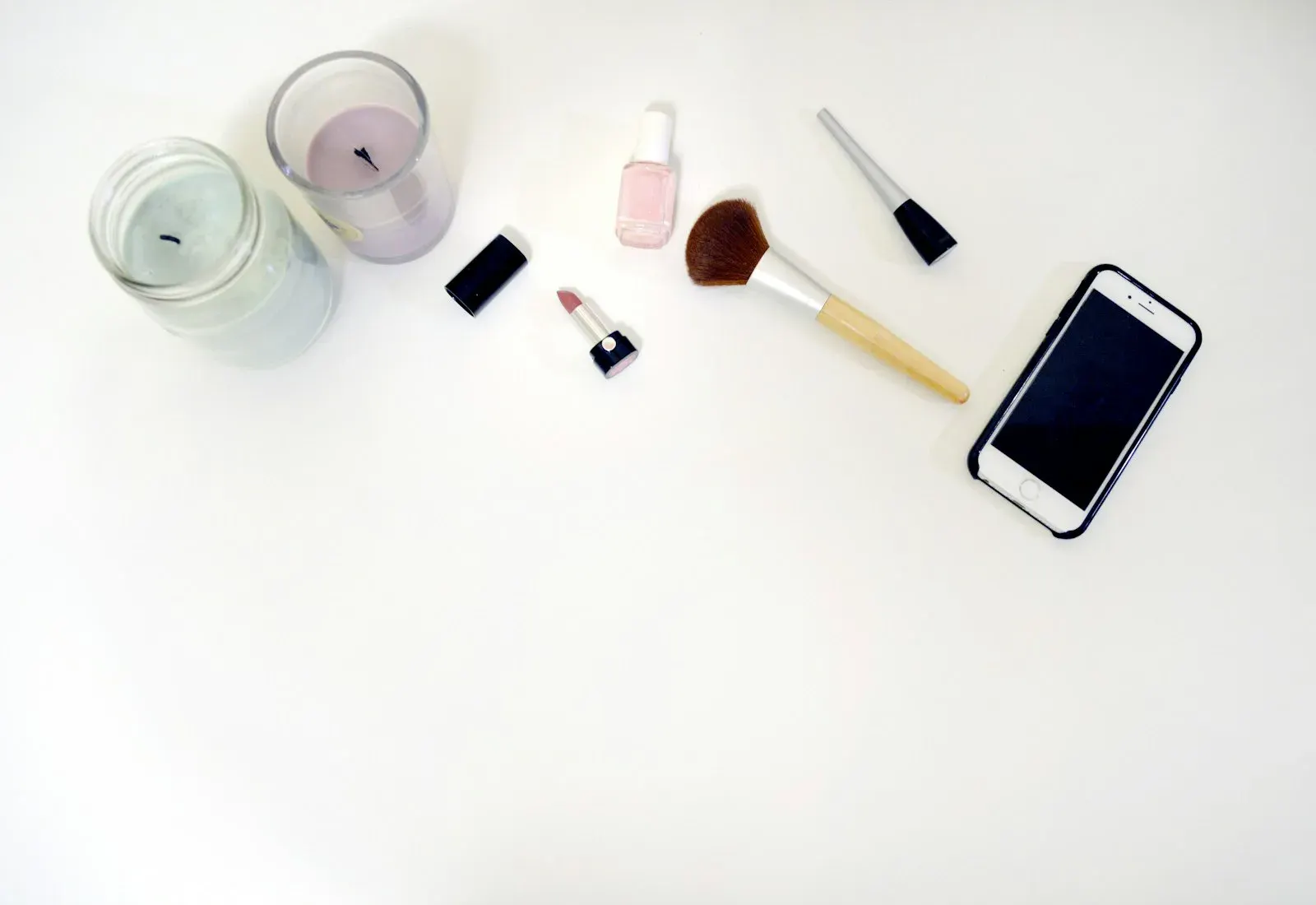 Candela profumata e piccoli accessori beauty disposti su un piano chiaro