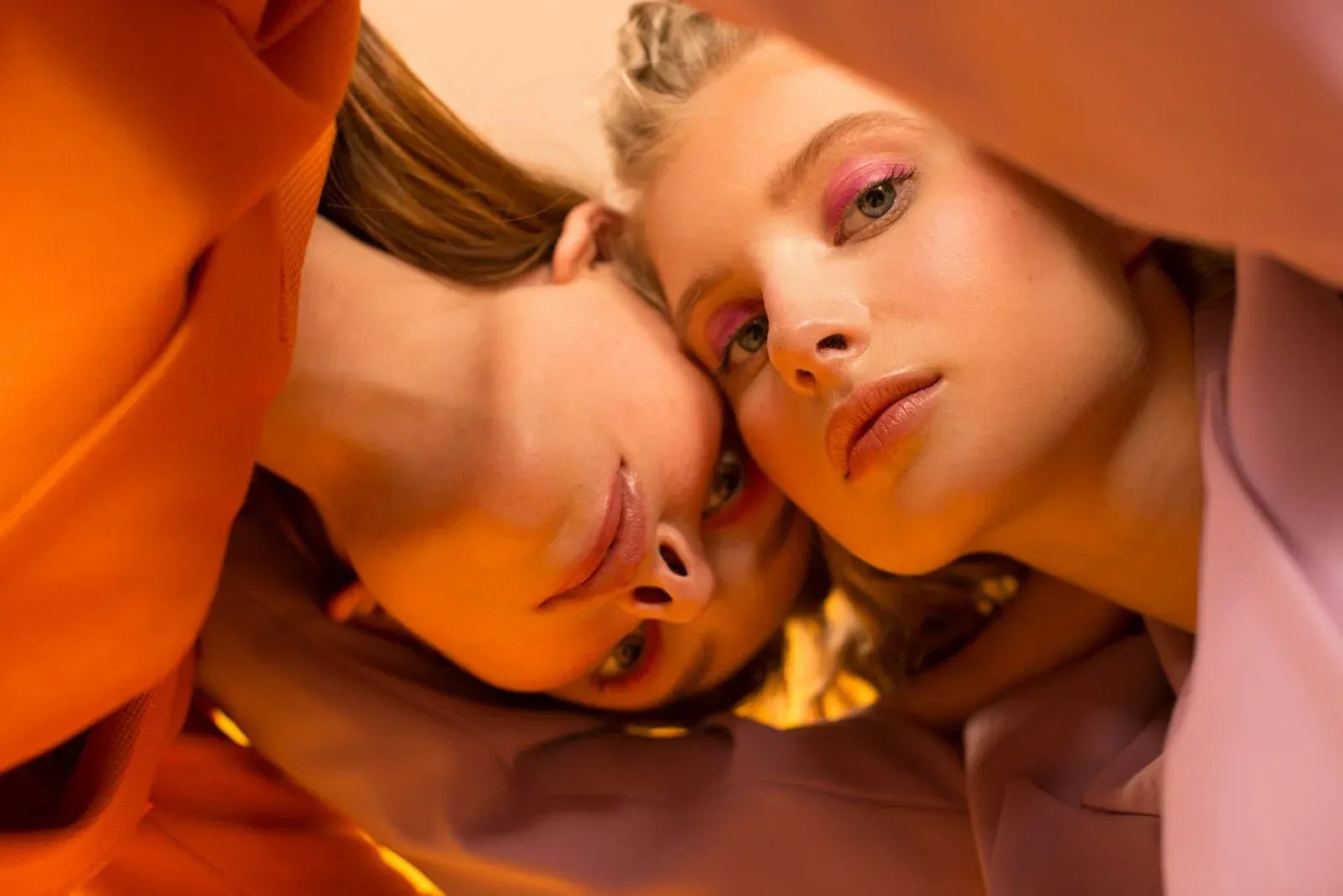 Backstage del lookbook, due modelle fianco a fianco tra tessuti arancio e rosa cipria