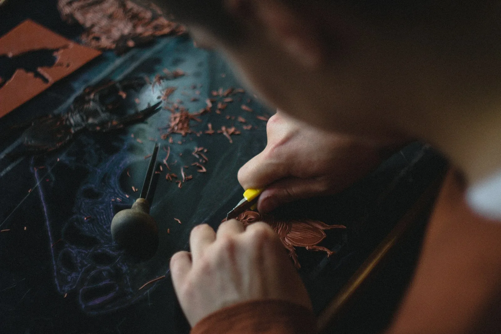 Le mani del maestro incidono a mano il disegno sul cuoio prima della cucitura, tra i trucioli lasciati dal bulino sul banco di lavoro